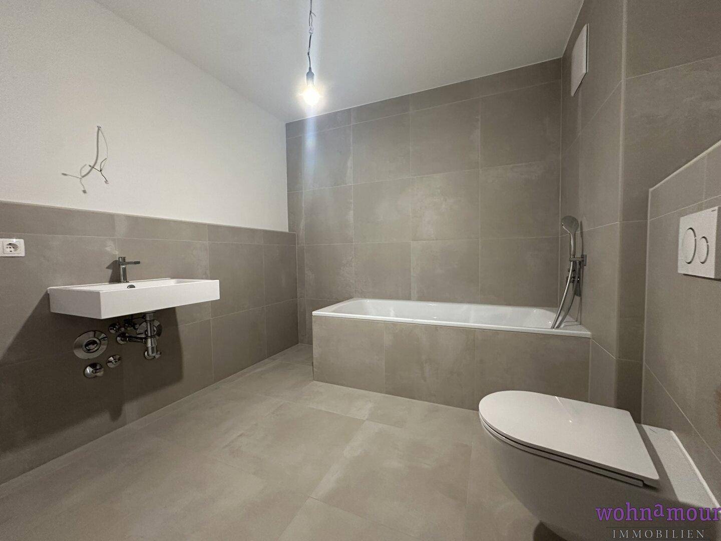 Modernes Badezimmer mit Badewanne, wandhängendem WC und eleganten grauen Fliesen.