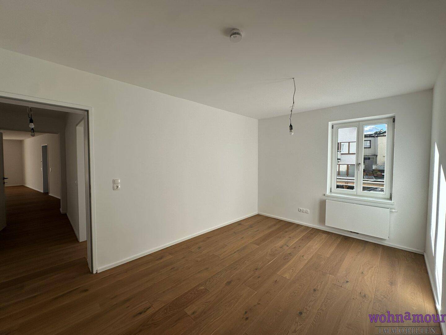 Helles Schlafzimmer mit Parkettboden und einem Fenster, das viel natürliches Licht hereinlässt.