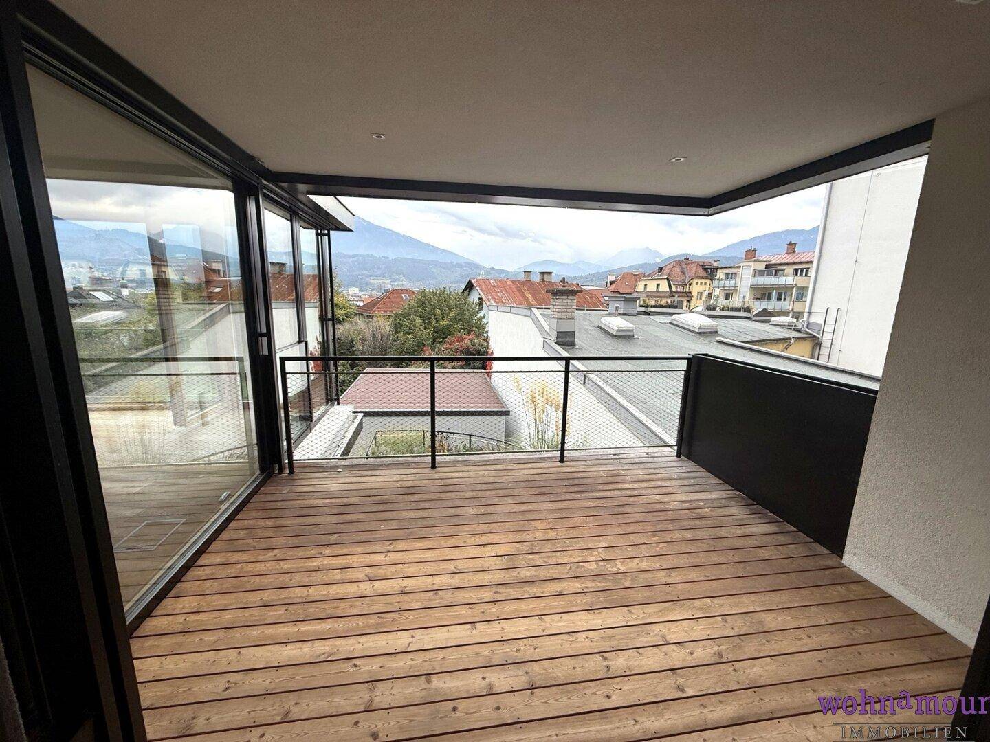 Heller Balkon mit Holzdielen und weitem Blick über die Dächer der Stadt und die Berglandschaft.