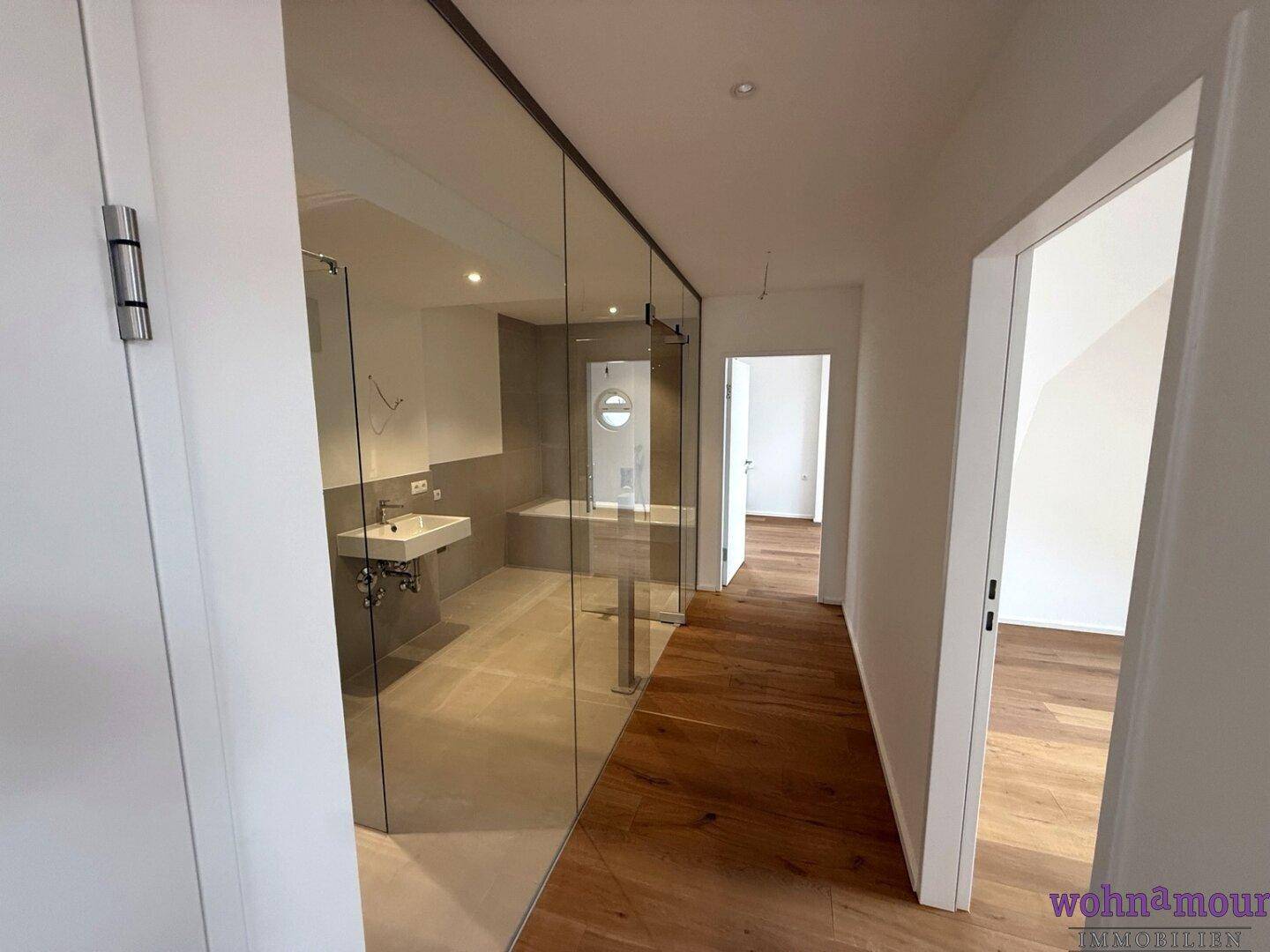 Heller Flur mit Holzboden, der zu einem modernen Badezimmer mit Glaswand führt.