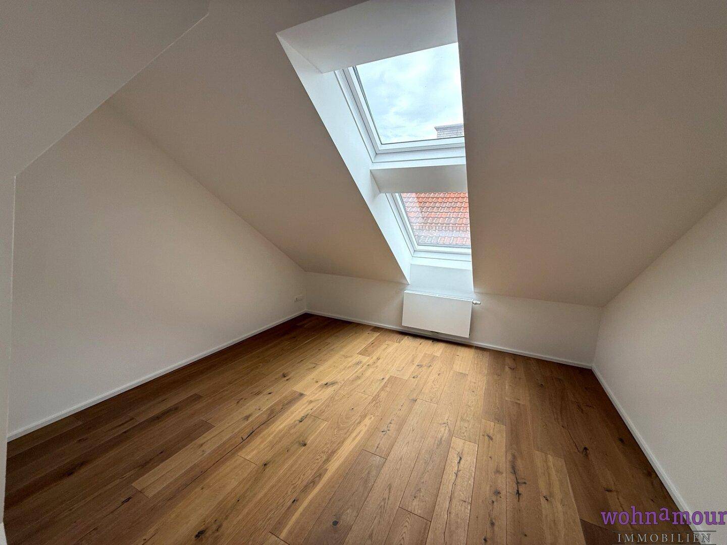Gemütliches Dachzimmer mit Holzboden und einem großen Dachfenster, das viel Tageslicht spendet.