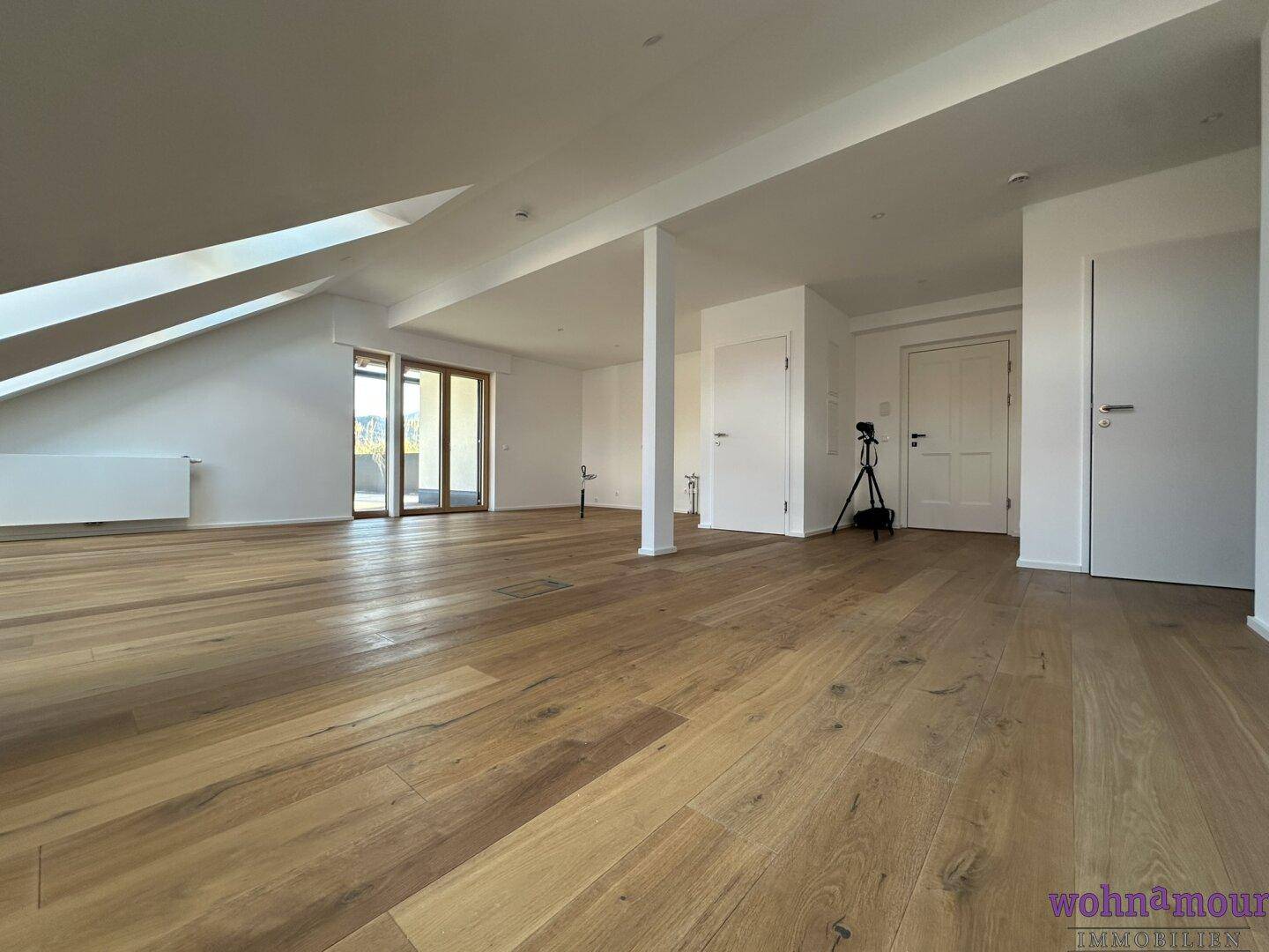 Geräumiger, heller Wohnbereich mit hochwertigem Holzboden und Zugang zu einer Außenterrasse.
