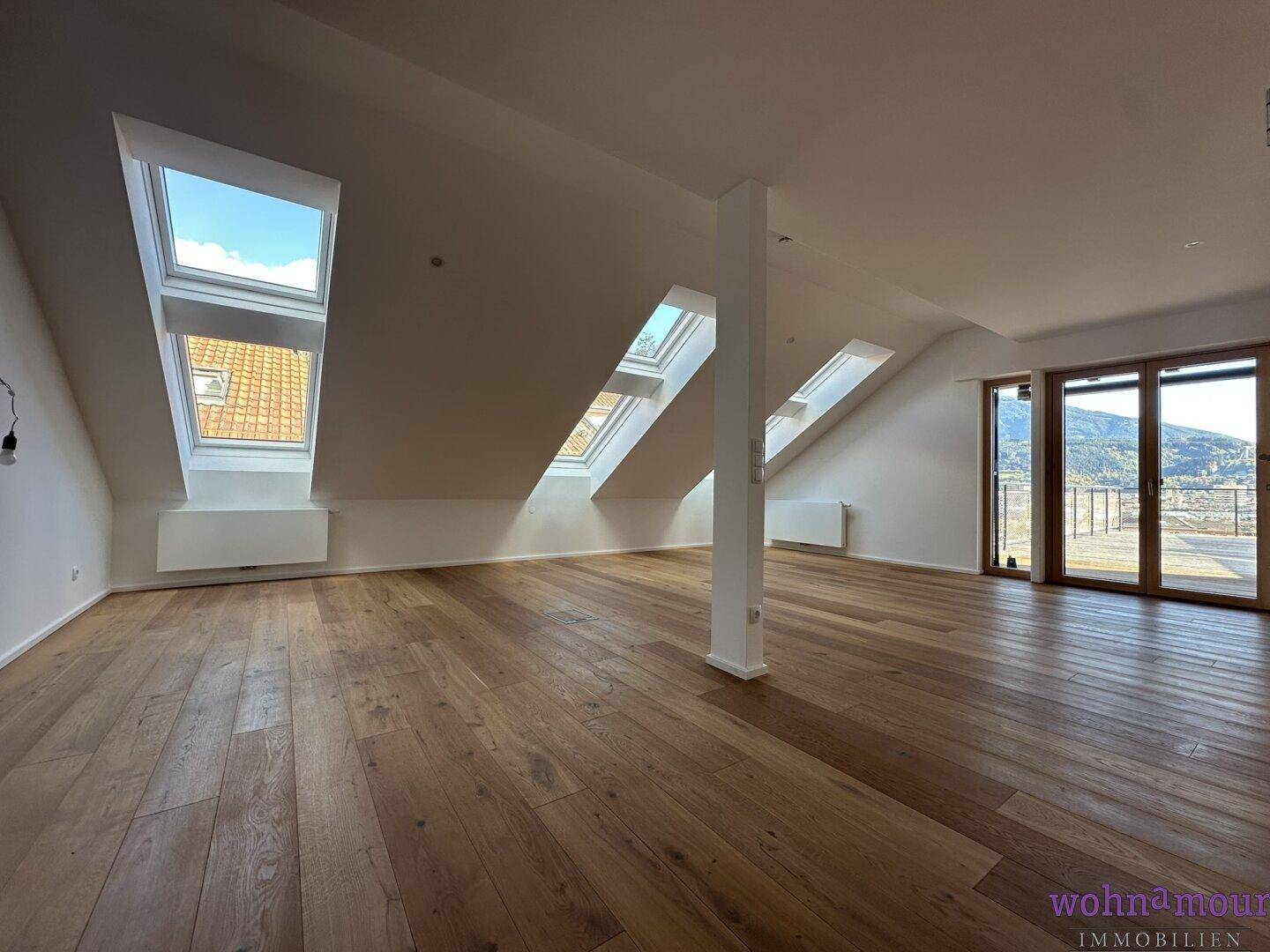 Lichtdurchfluteter Wohnraum im Dachgeschoss mit mehreren Dachfenstern und Holzboden.