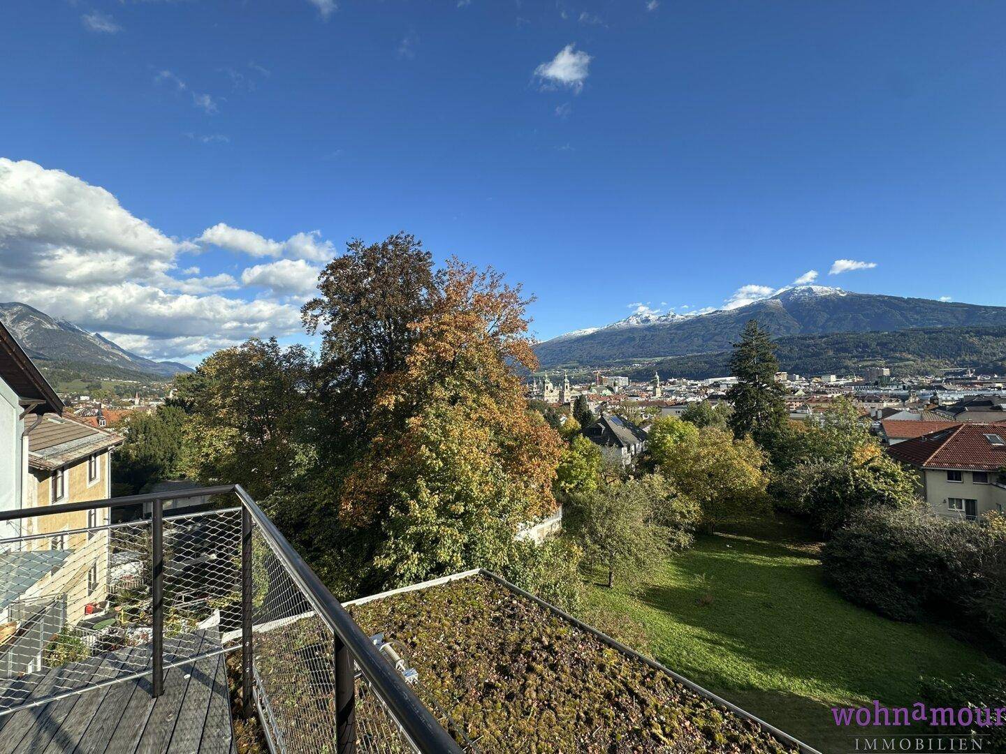 Panoramablick von der Terrasse über die grüne Landschaft, die Stadt und die schneebedeckten Berge.