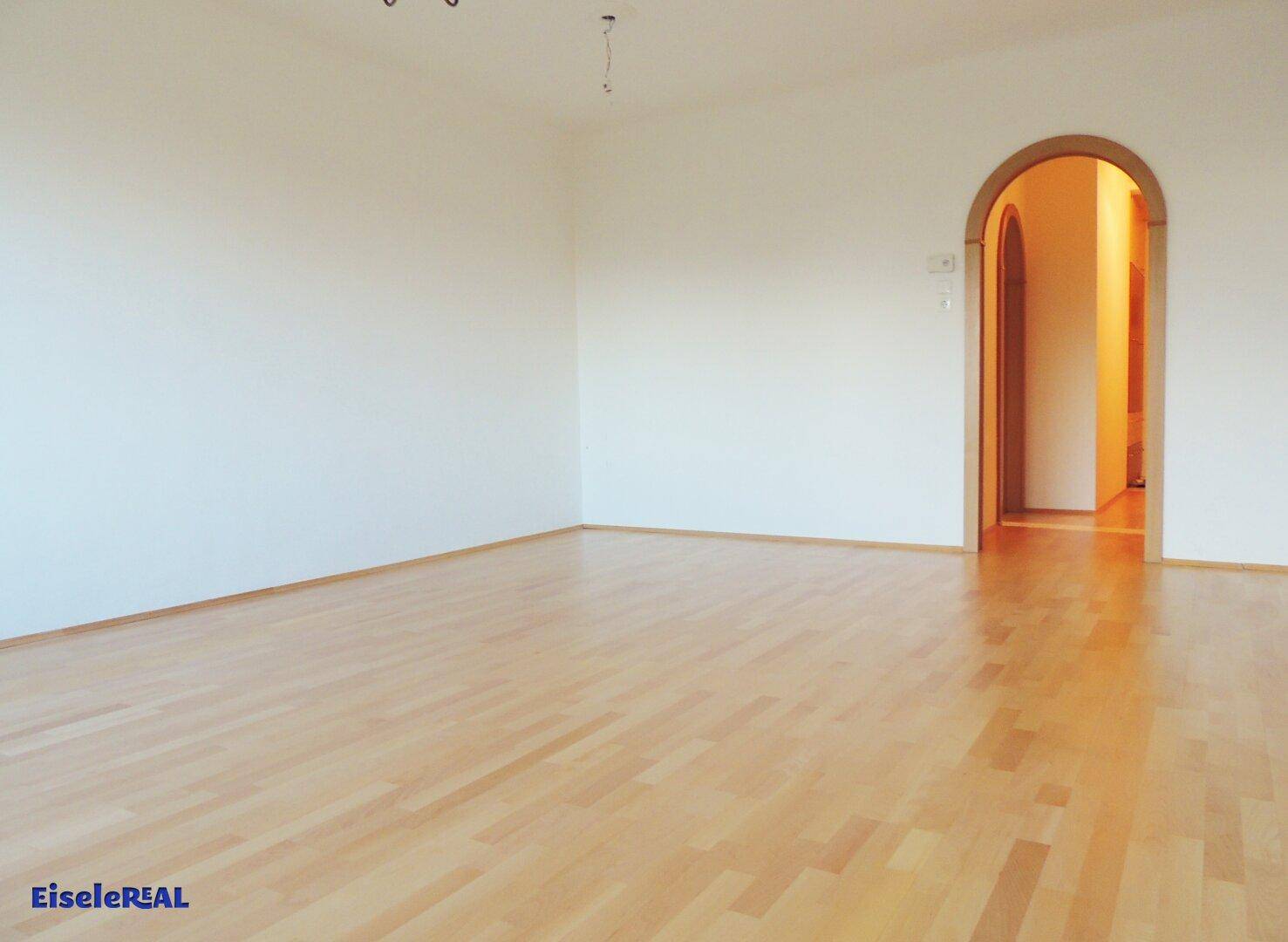 Geräumiges Wohnzimmer mit hellem Parkettboden und einem eleganten Rundbogen zu einem weiteren Raum.