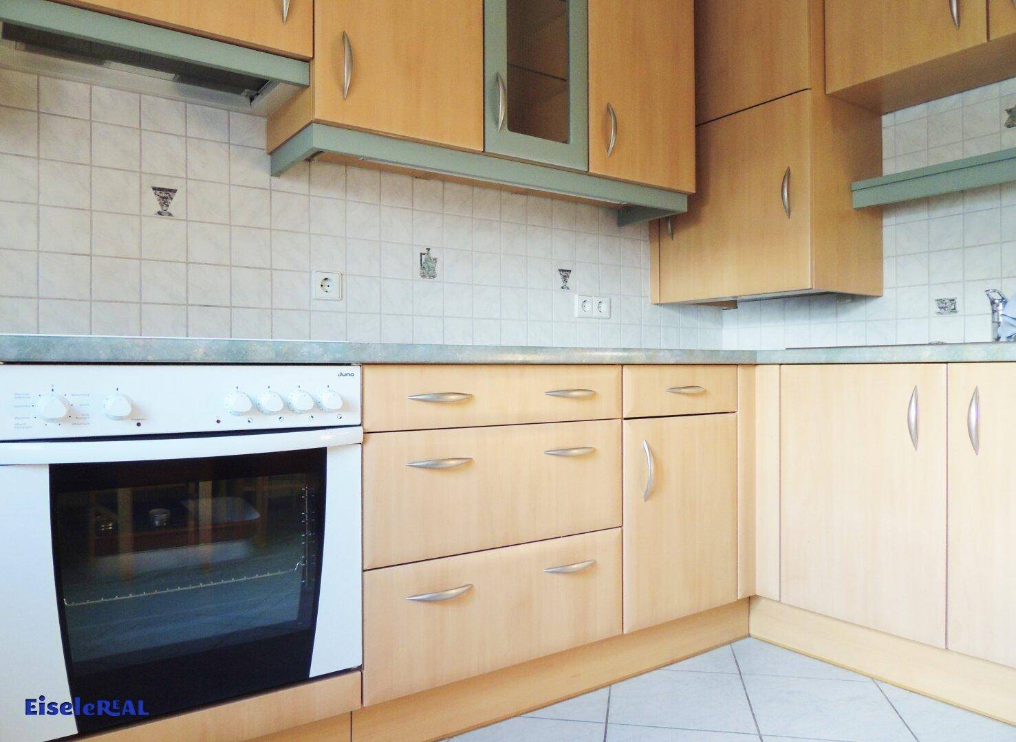 Funktionale Küche mit hellen Holzschränken, Elektroherd und gefliestem Spritzschutz.