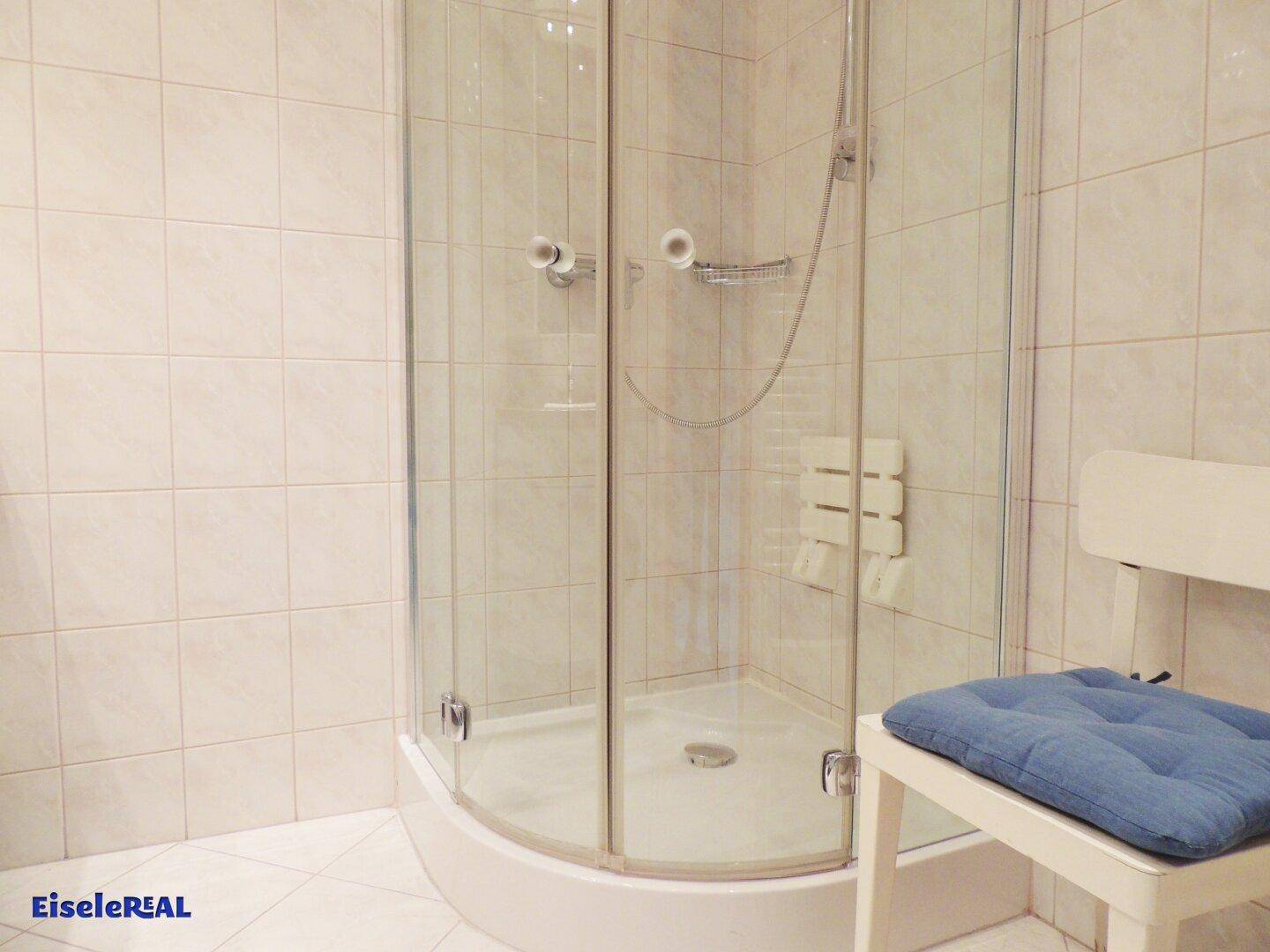 Badezimmer mit Duschkabine, hellen Fliesen und einem kleinen Hocker.