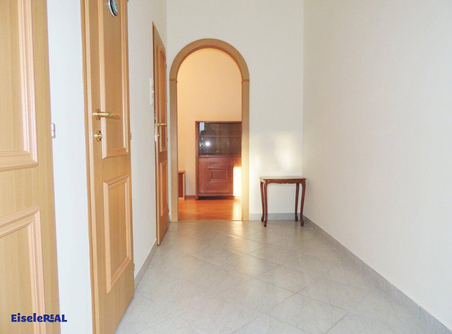 Eingangsbereich mit Fliesenboden, einem dekorativen Beistelltisch und einem Rundbogen zu einem weiteren Raum.