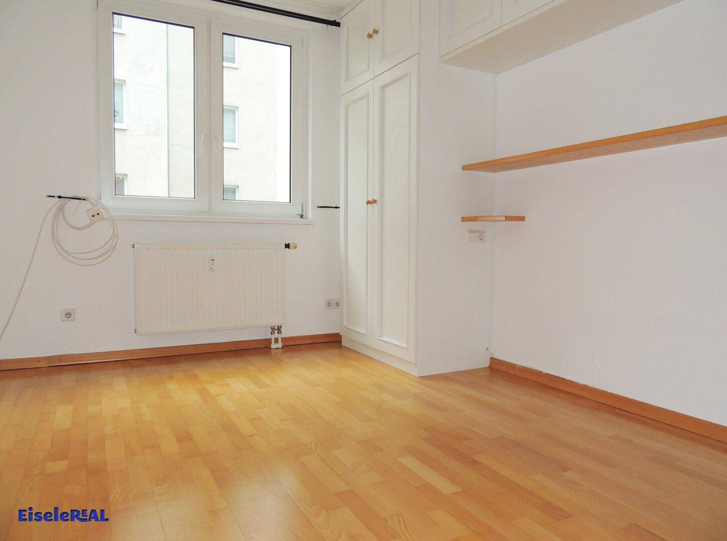 Helles Zimmer mit Parkettboden, Fenster und praktischen Einbauschränken für Stauraum.
