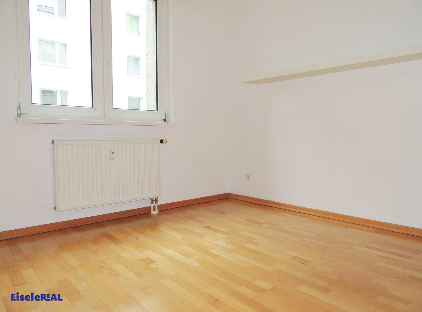 Leeres Zimmer mit Parkettboden und einem großen Fenster, das für viel Helligkeit sorgt.