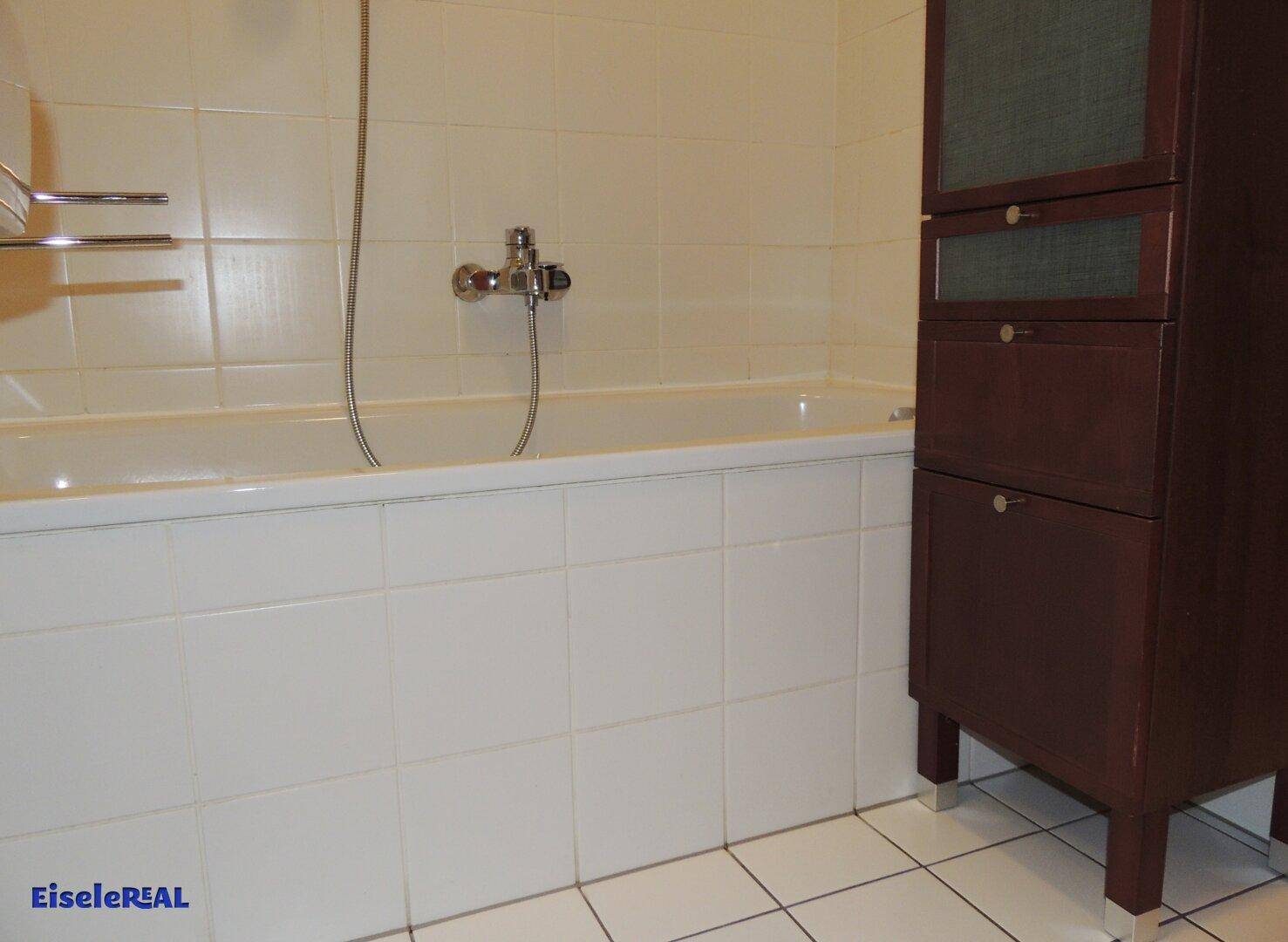 Badezimmer mit Badewanne, weißen Fliesen und einem dunklen Holzschrank.