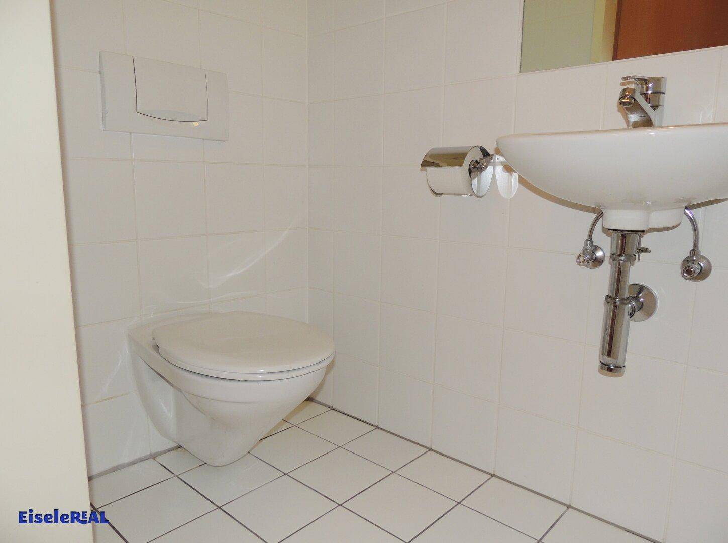 Separate Toilette mit wandhängendem WC, Waschbecken und weißen Fliesen.