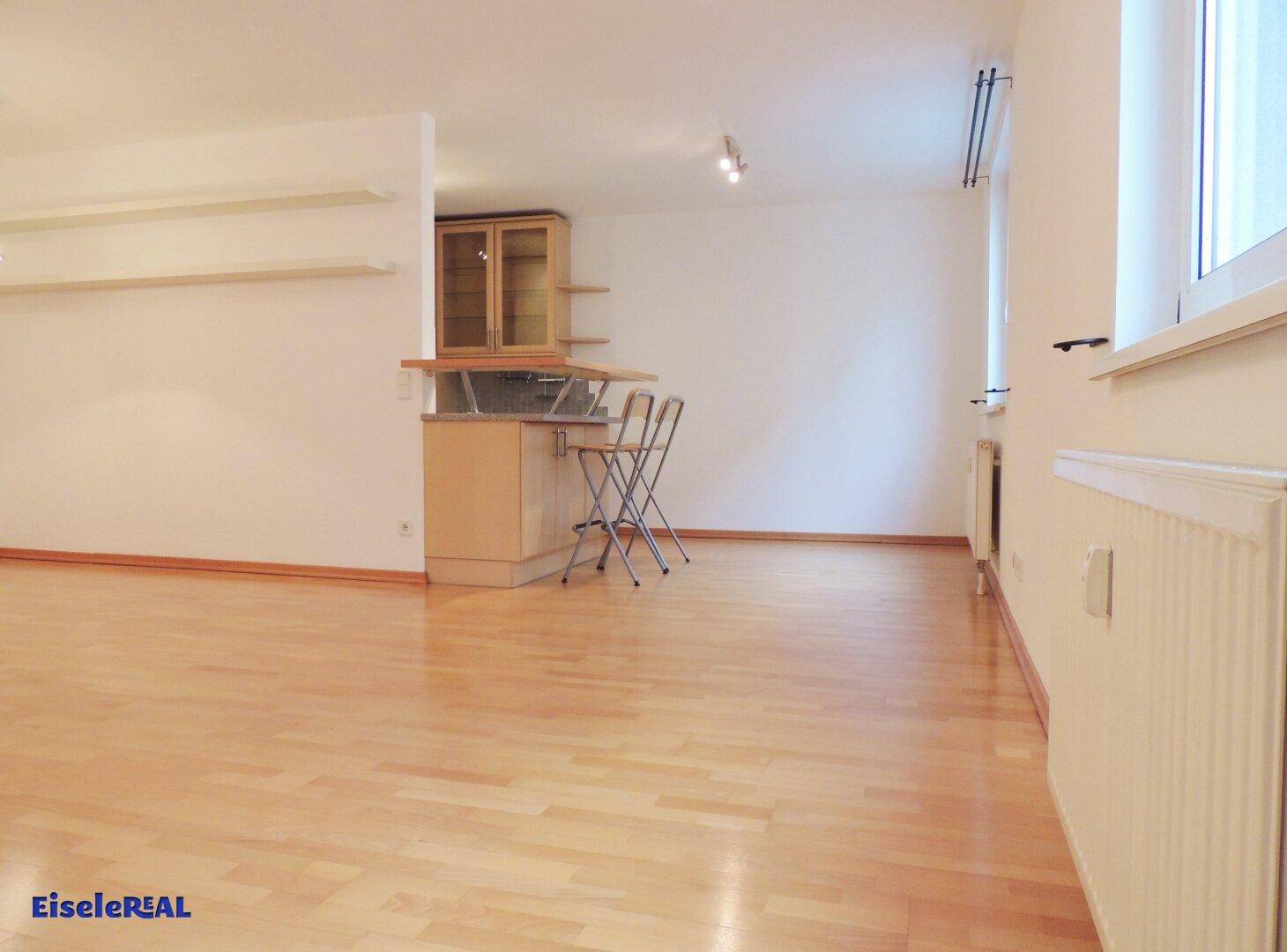 Geräumiger Wohnbereich mit Parkettboden und einer integrierten Bar mit Hockern.