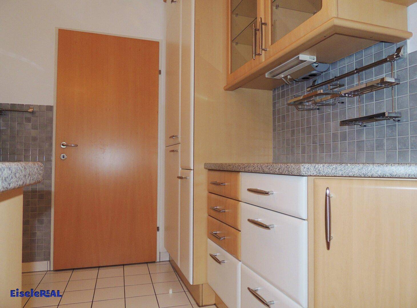 Küchenzeile mit hellen Holzschränken, Fliesenboden und ausreichend Stauraum.