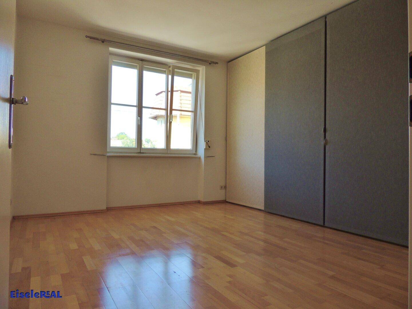 Leeres Schlafzimmer mit Parkettboden, großem Fenster und praktischen Einbauschränken.
