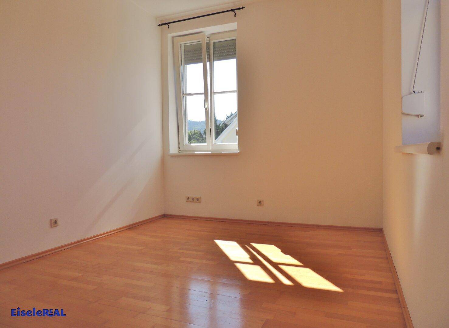 Sonniger Raum mit Parkettboden und einem Fenster, das viel Tageslicht hereinlässt.