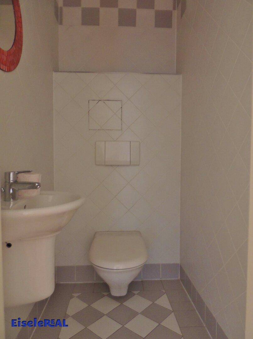 Separates WC mit wandhängender Toilette, Waschbecken und Fliesenboden.