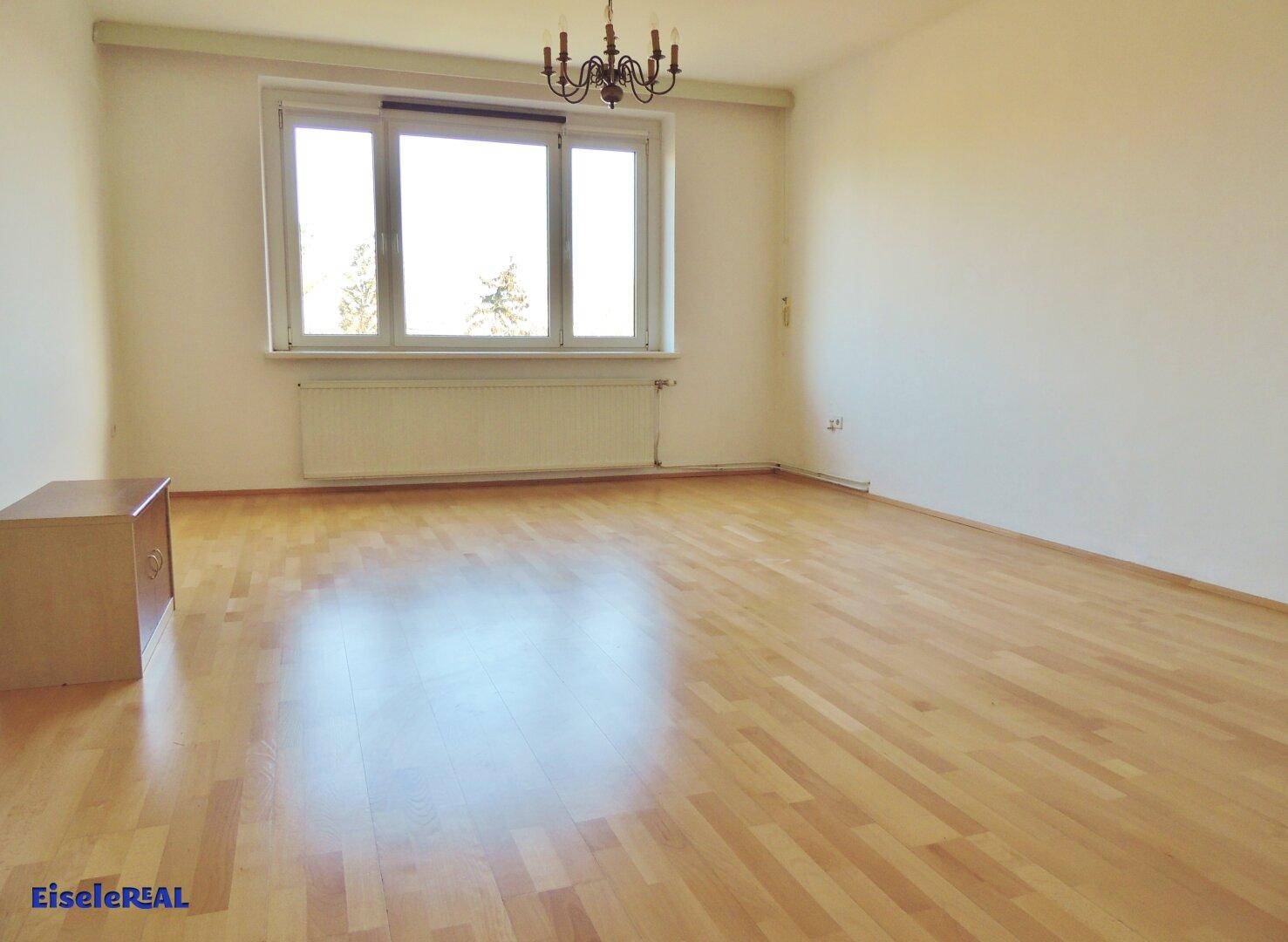 Helles, leeres Wohnzimmer mit Parkettboden und großem Fenster, bereit zur Einrichtung.