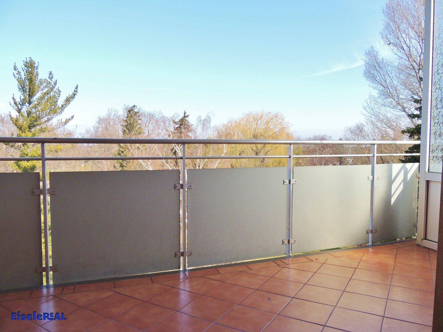 Geräumiger Balkon mit Fliesenboden und Blick ins Grüne, umgeben von Bäumen.