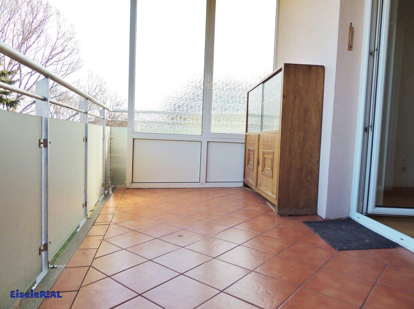 Balkon mit Terrakotta-Fliesen, einem alten Holzschrank und Zugang zu einem Innenraum.