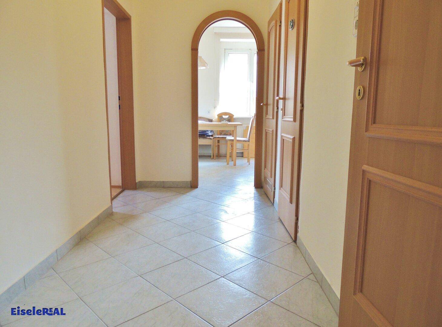 Heller Flur mit Fliesenboden und einem Rundbogen, der zu einem Essbereich führt.