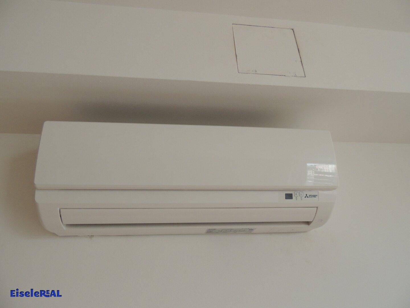 Eine weiße Klimaanlage ist unter einer Deckenverkleidung an einer hellen Wand montiert, in einem sauberen und funktionsfähigen Zustand.