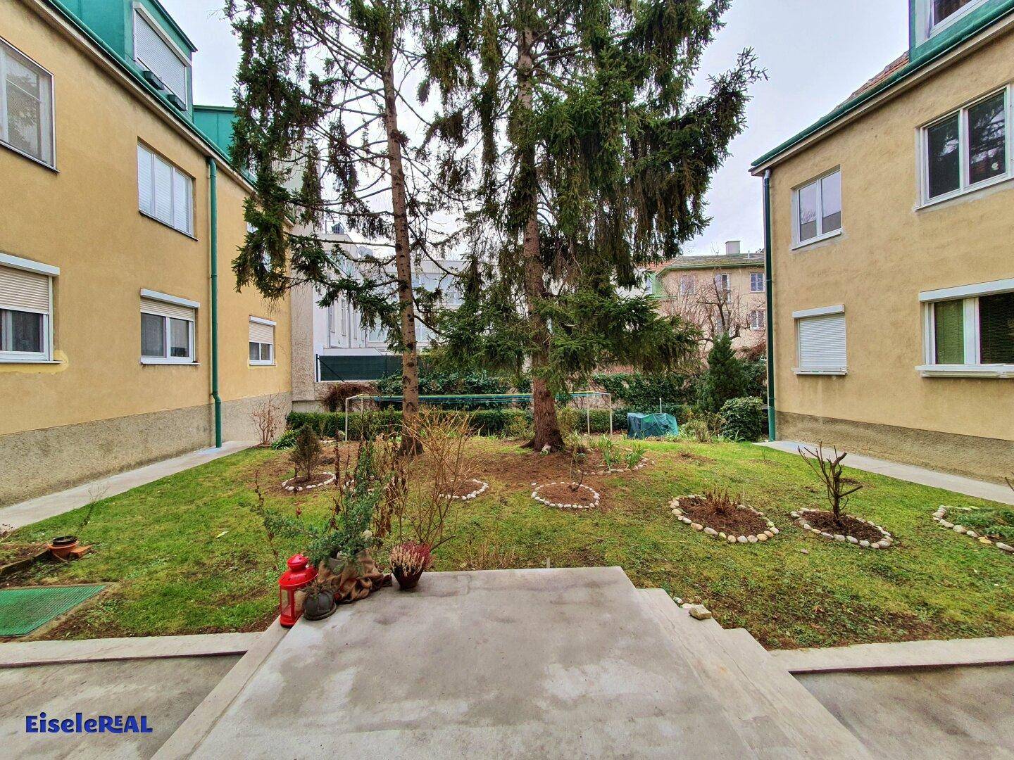 Gepflegter Gemeinschaftsgarten mit Rasenfläche und Bäumen zwischen Wohngebäuden.