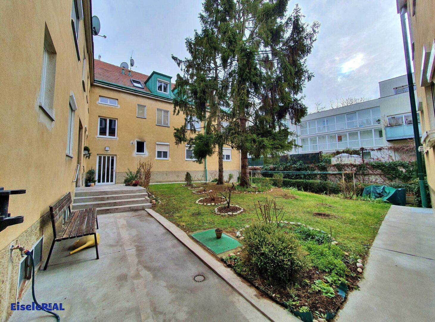 Ruhiger Innenhof mit Grünfläche, Sitzbank und Zugang zu den Wohnungen.
