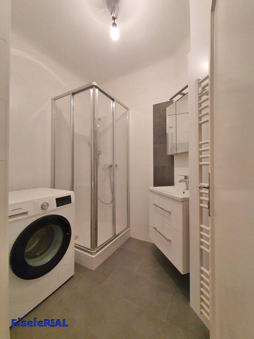 Modernes Badezimmer mit Duschkabine, Waschbecken, beheiztem Handtuchhalter und Waschmaschine.