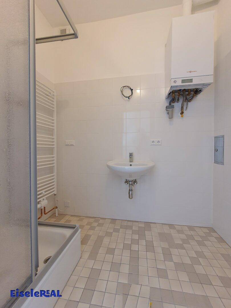 Badezimmer mit Duschkabine, Waschbecken und Heizkörper, ausgestattet mit weißen Fliesen und einem Gasboiler.