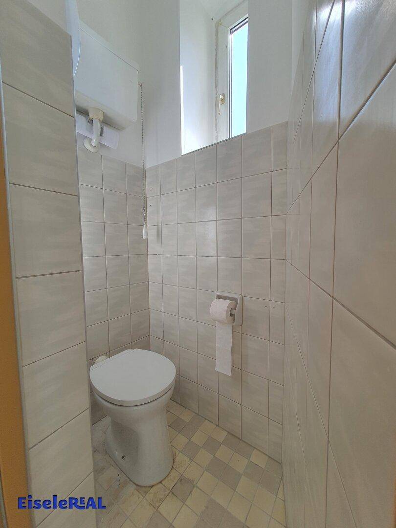 Separate Toilette mit WC, gefliesten Wänden und einem kleinen Fenster für Belüftung und Tageslicht.