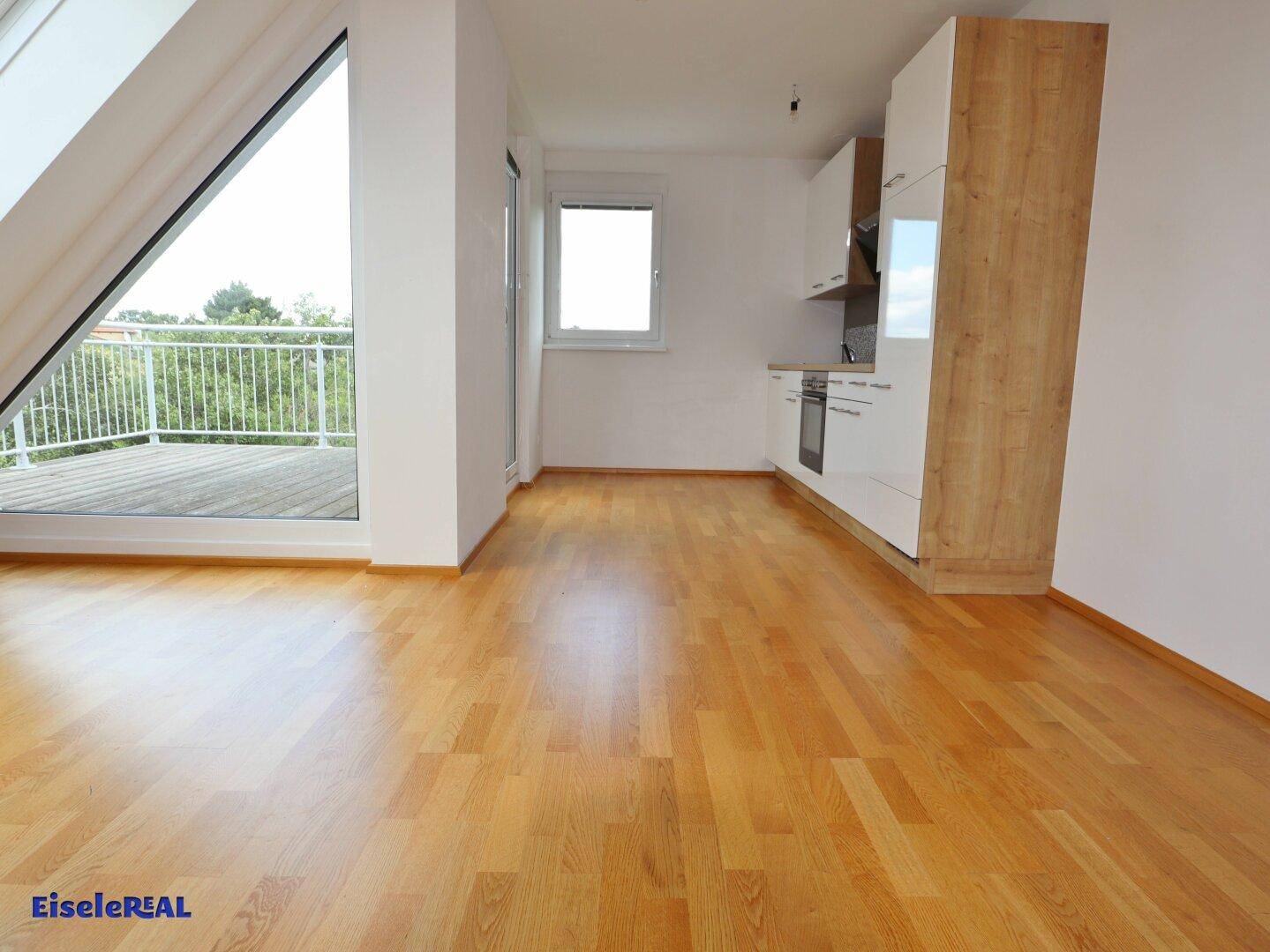 Heller Wohnbereich mit Holzboden, Dachschräge und Zugang zu einem Balkon.