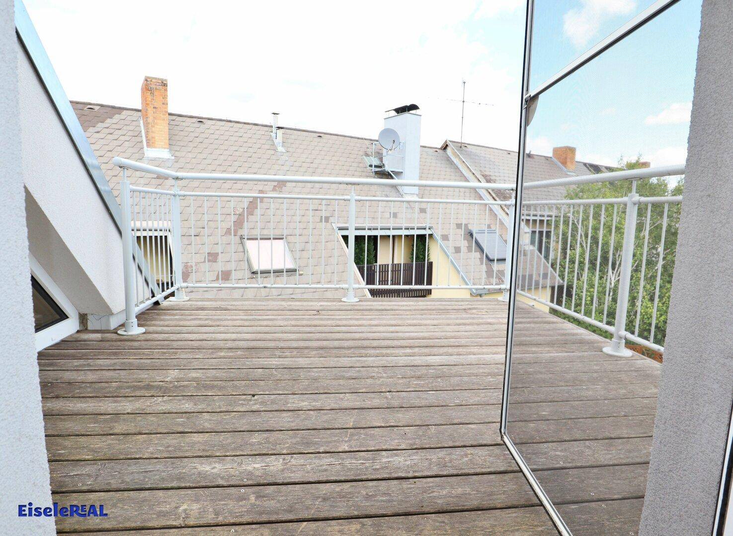 Geräumiger Balkon mit Holzdielen und Blick auf die umliegenden Dächer und Bäume.