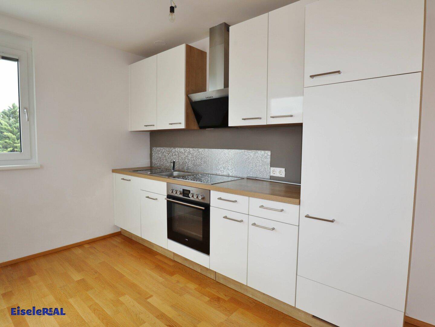 Moderne Einbauküche mit weißen Fronten, Holzarbeitsplatte und Fenster.