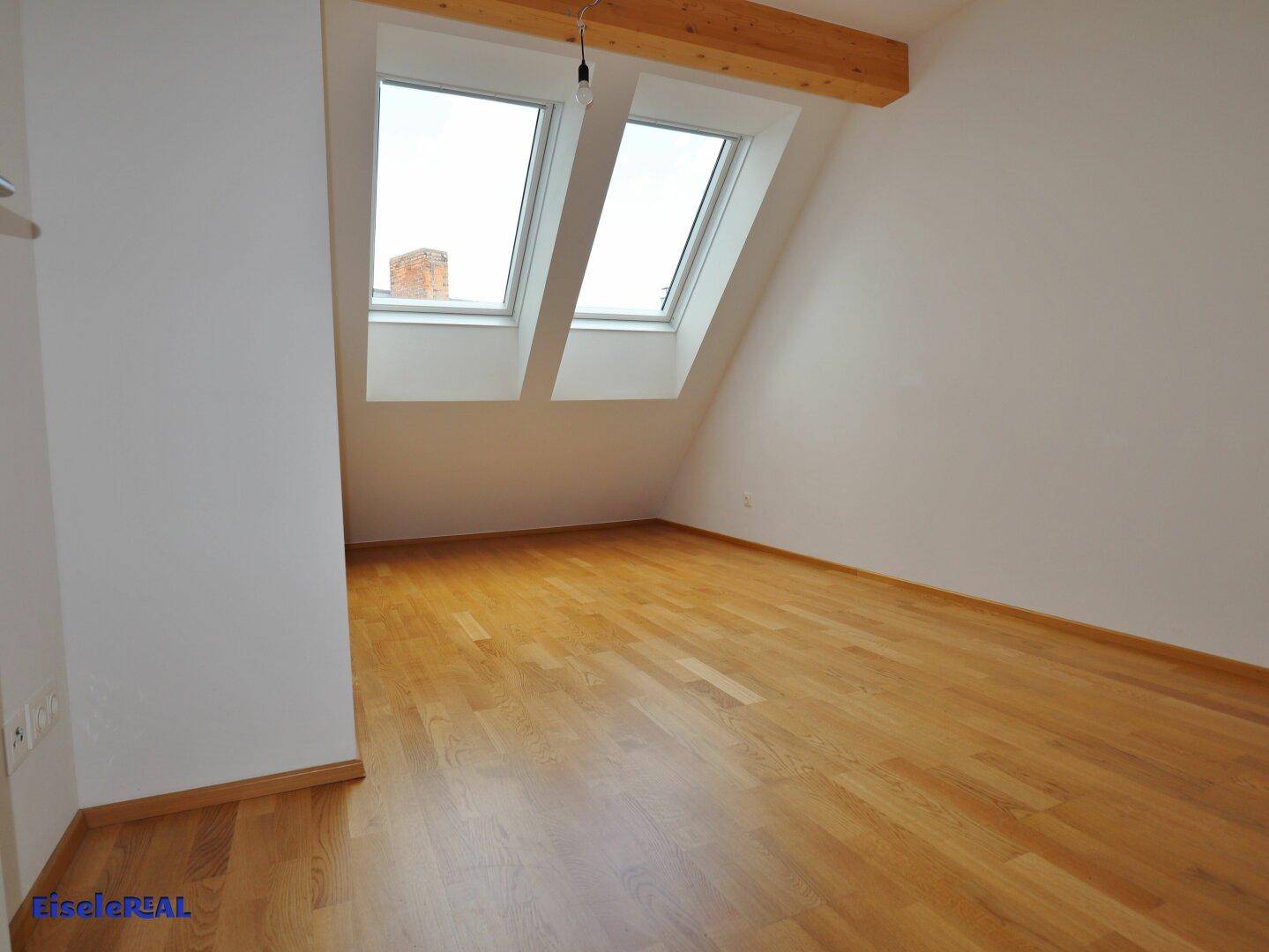 Helles Zimmer mit Holzboden, Dachschräge und zwei großen Dachfenstern.