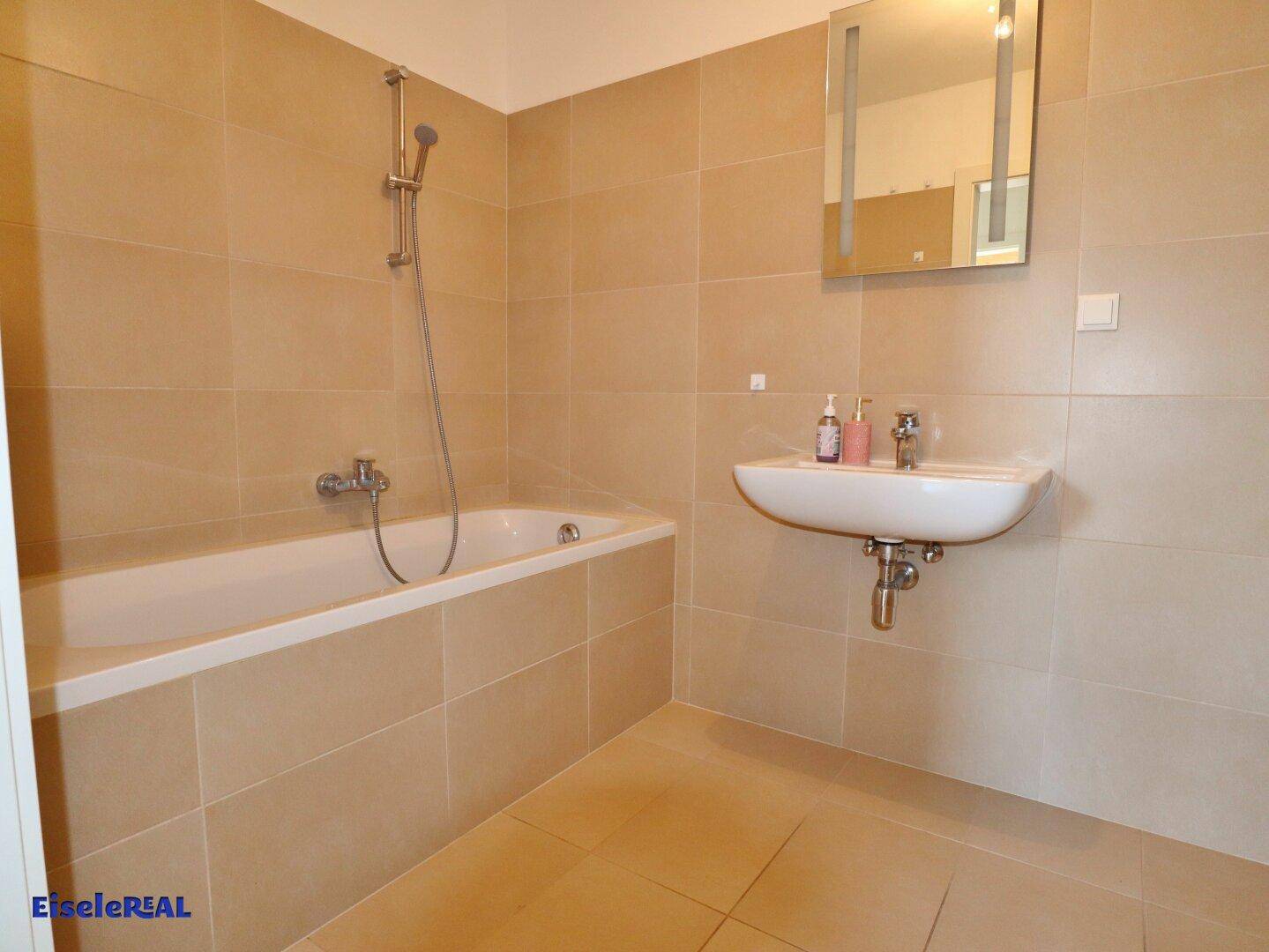 Modernes Badezimmer mit Badewanne, Waschbecken und hellen Fliesen.