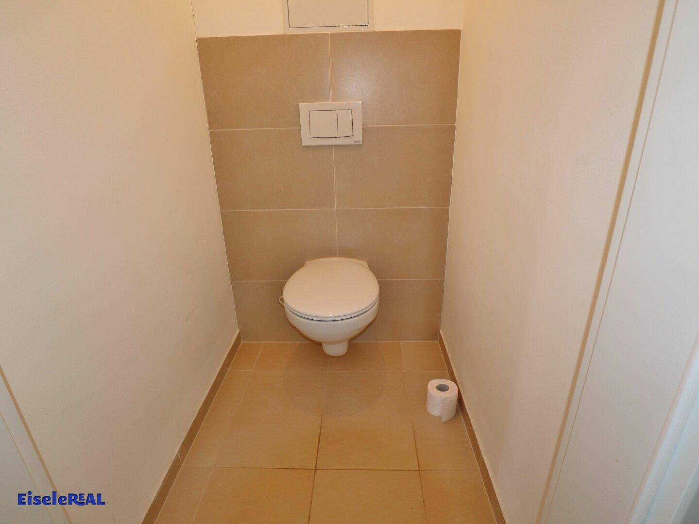 Separates WC mit wandhängender Toilette und hellen Fliesen.