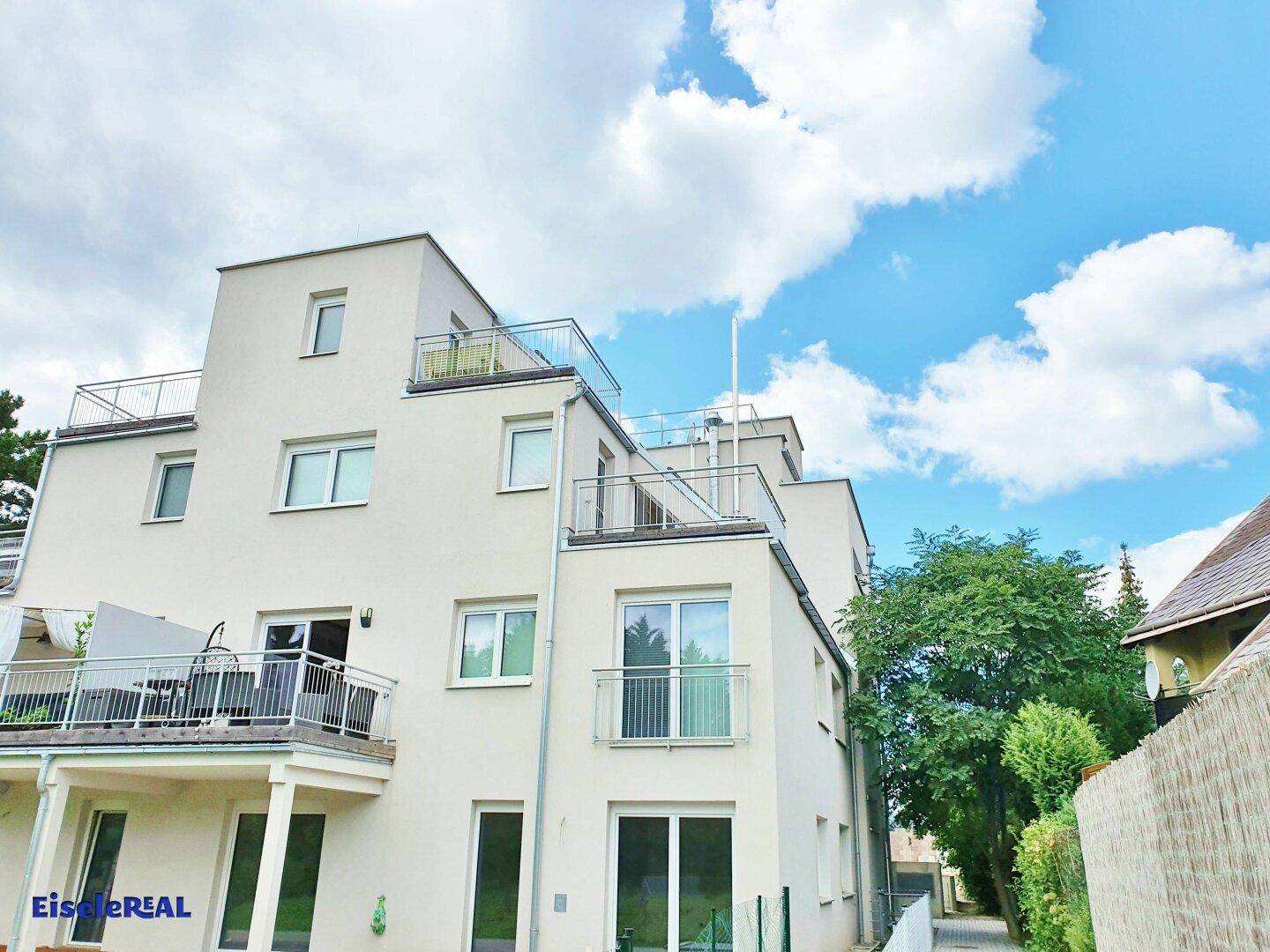 Rückansicht des modernen Mehrfamilienhauses mit Balkonen und Dachterrassen.