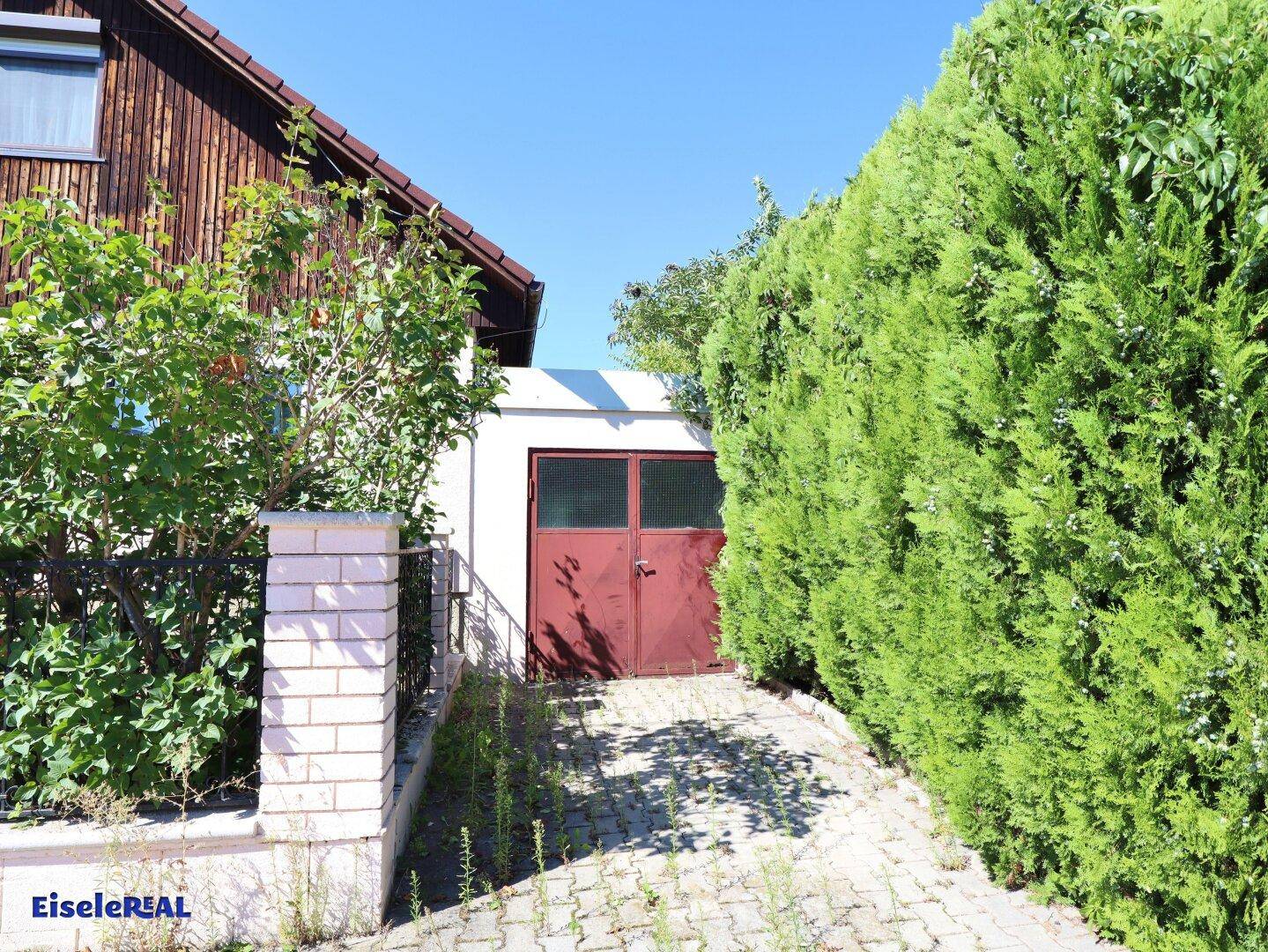Garagenzufahrt mit hohen Hecken und einem roten Garagentor an der Seite des Hauses.
