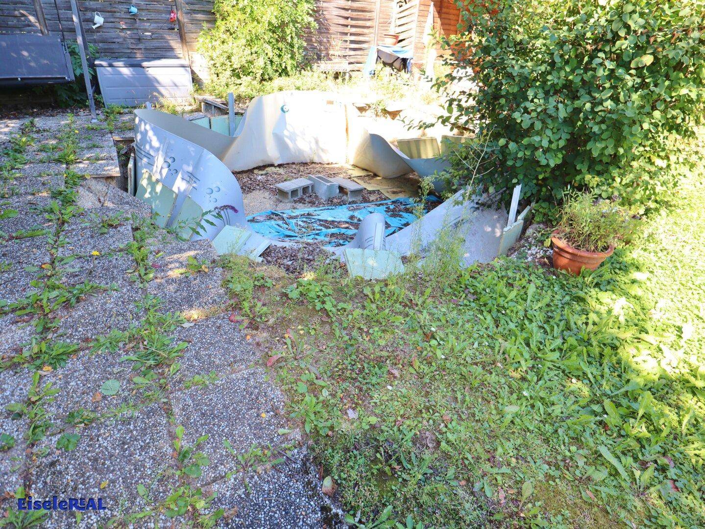 Gartenbereich mit einer unfertigen oder abgebauten Poolstruktur und Steinplatten.