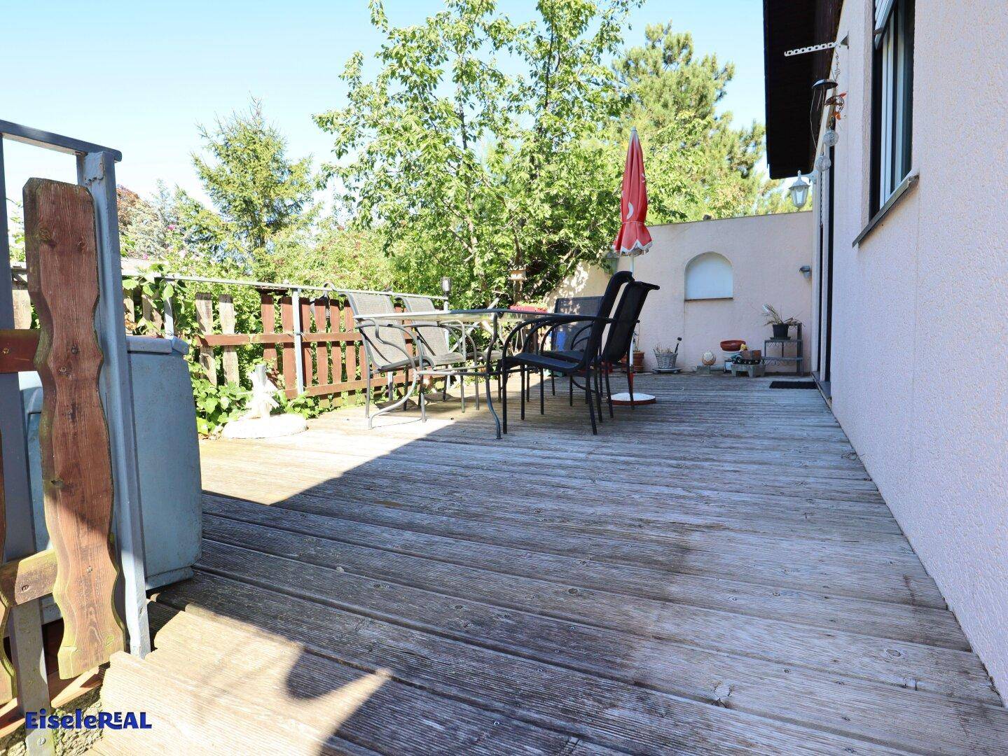 Geräumige Holzterrasse mit Gartenmöbeln und einem Sonnenschirm, ideal für Mahlzeiten im Freien.