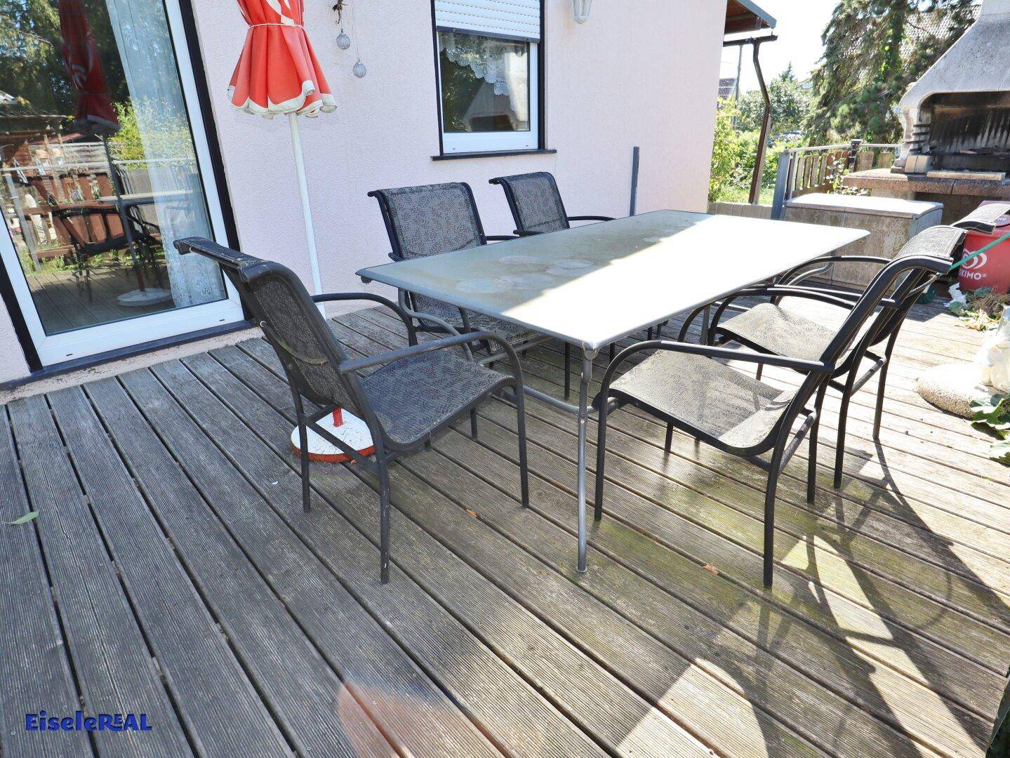 Holzterrasse mit großem Esstisch und Stühlen, bereit für gesellige Stunden im Freien.