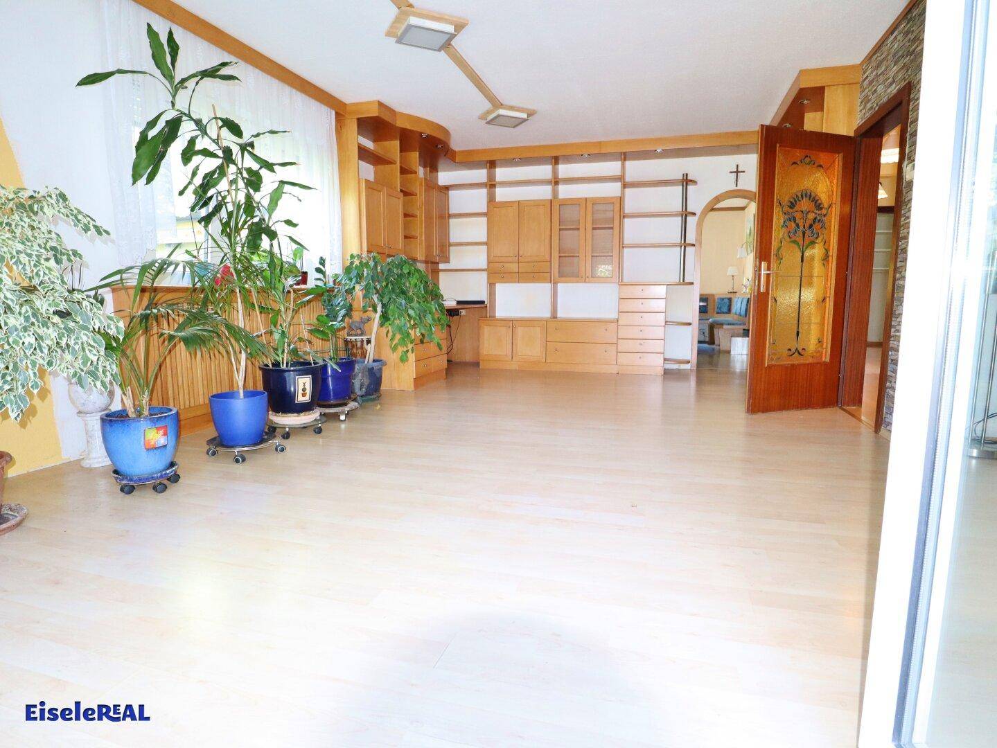 Großzügiges Wohnzimmer mit Einbauschränken aus Holz und vielen Zimmerpflanzen, hell und einladend.