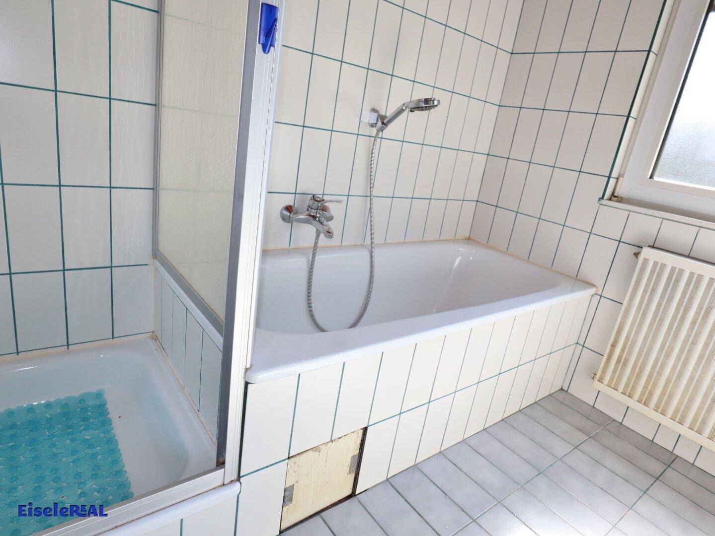 Badezimmer mit Badewanne und Duschbereich, ausgestattet mit weißen Fliesen und Fenster.
