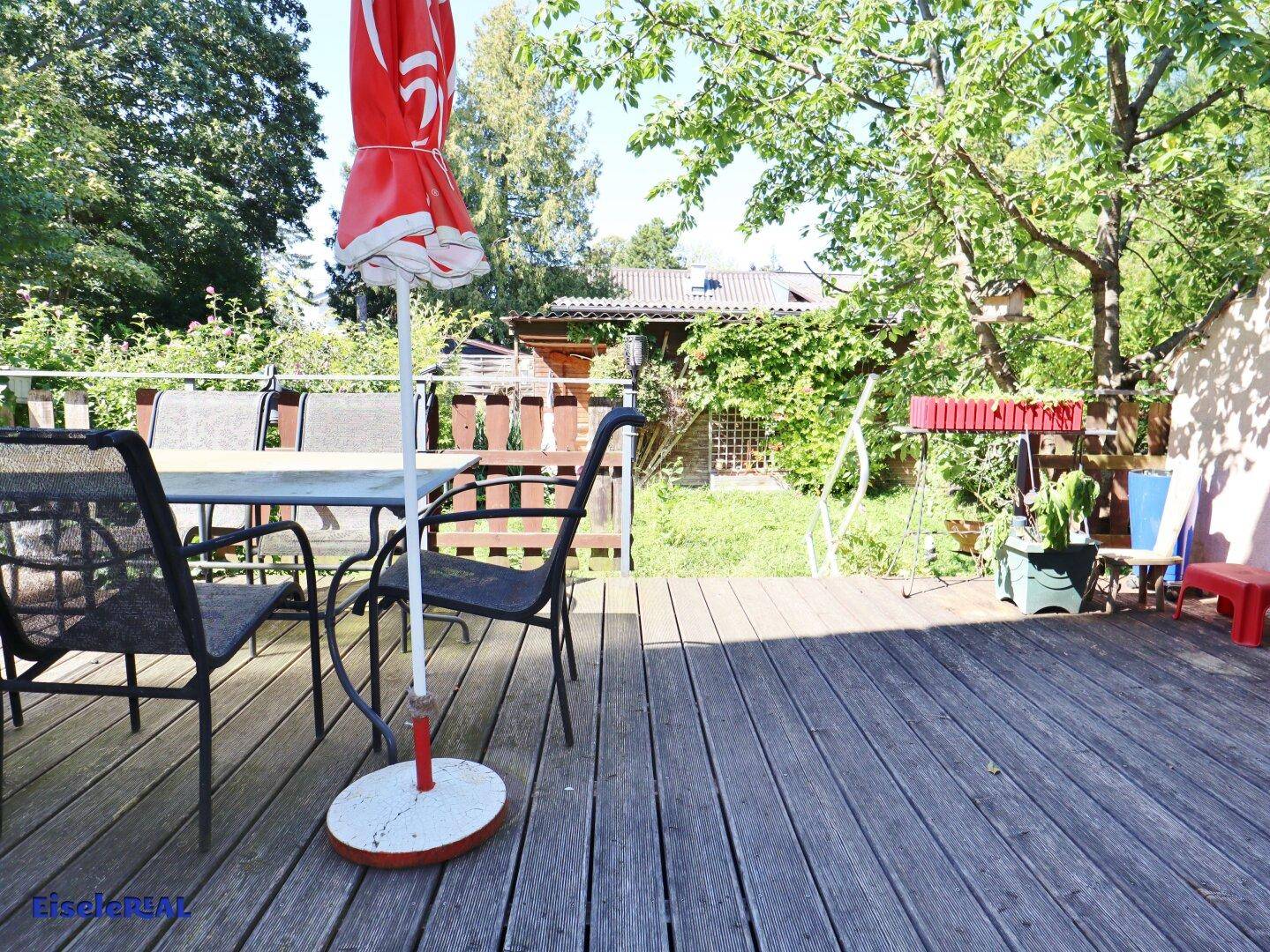 Holzterrasse mit Gartenmöbeln und Blick auf den grünen Gartenbereich mit Bäumen.