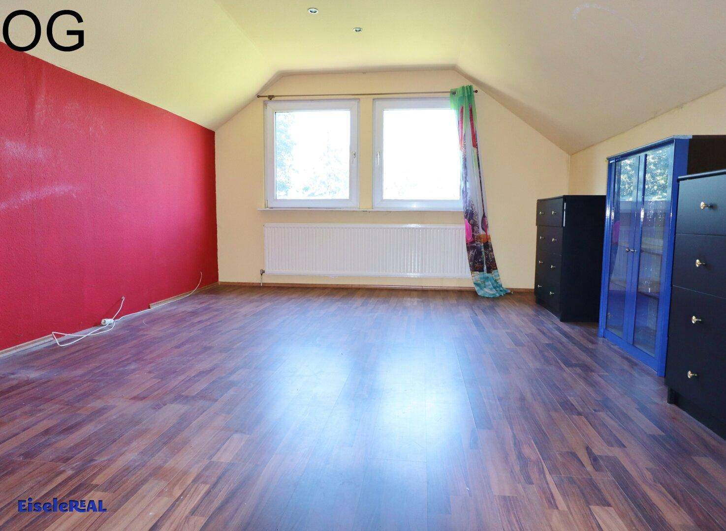 Schlafzimmer im Obergeschoss mit roter Akzentwand und dunklem Laminatboden, hell und geräumig.