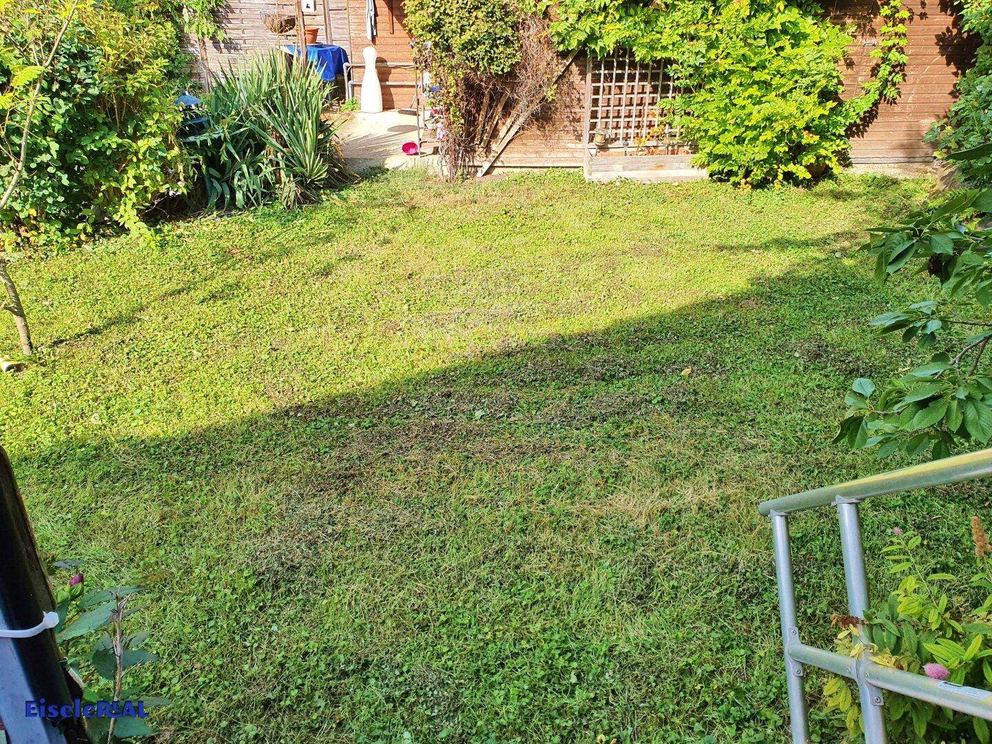 Grüner Gartenbereich mit Rasenfläche und Treppe, umgeben von üppiger Vegetation.