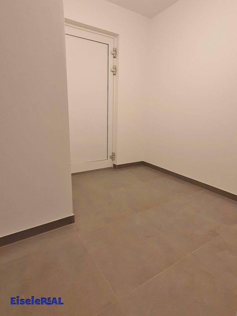 Leerer Raum mit hellen Wänden und grauen Fliesen, bereit für die individuelle Gestaltung.