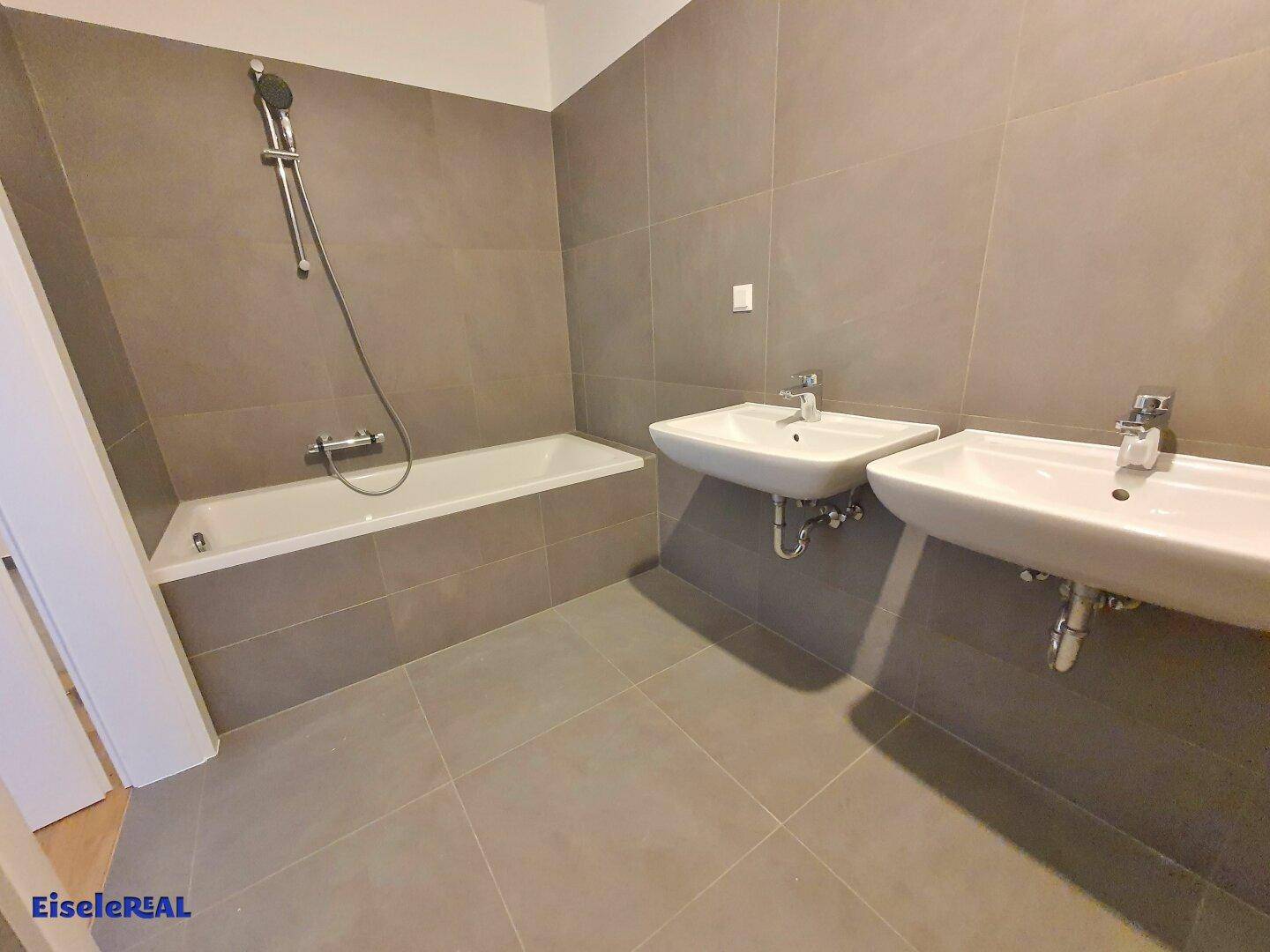 Modernes Badezimmer mit Badewanne, Doppelwaschbecken und grauen Fliesen.
