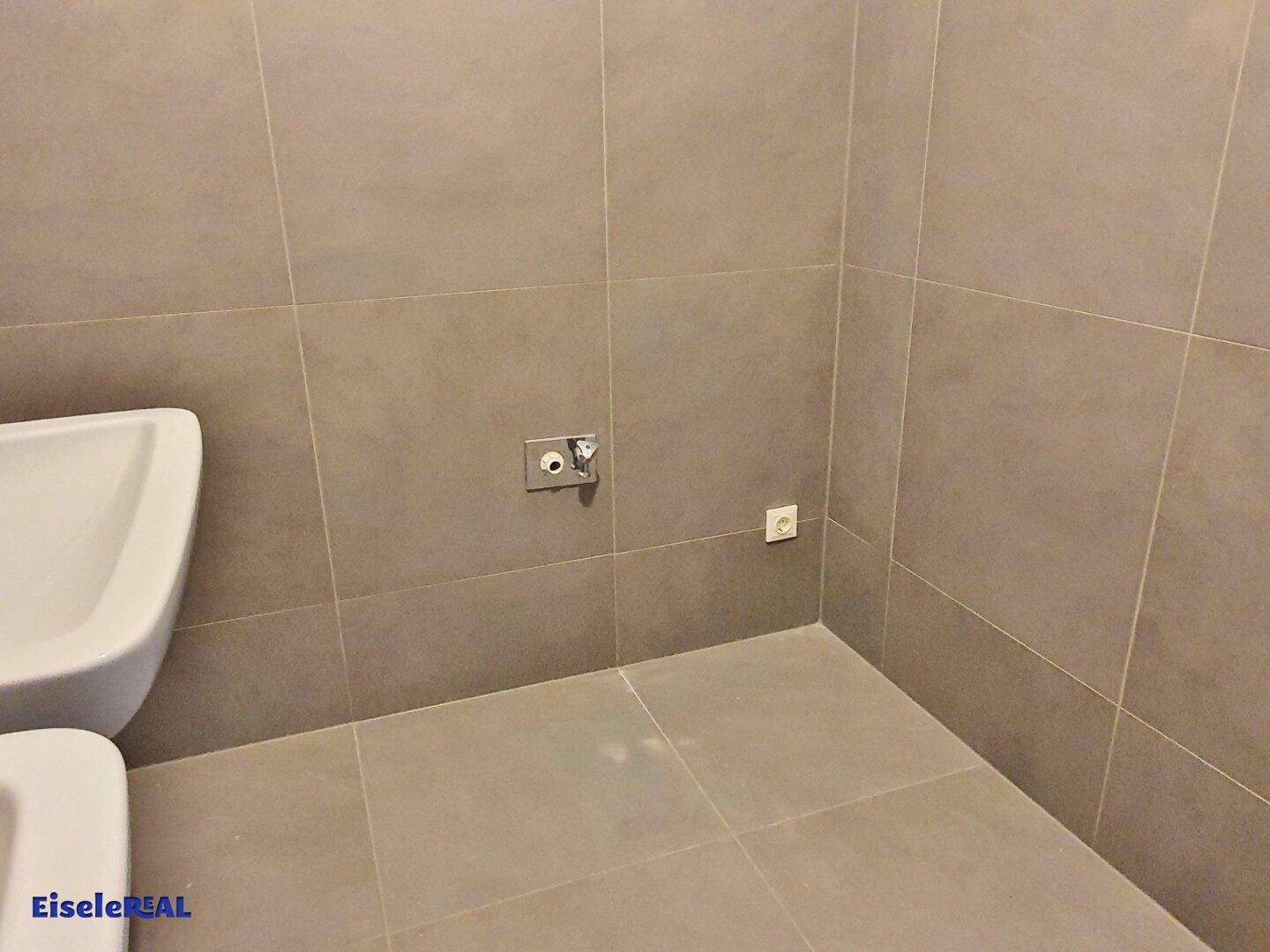 Detailansicht des Badezimmers mit grauen Fliesen und Anschlüssen für weitere Sanitärobjekte.
